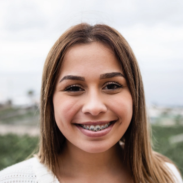 Young woman smiling at camera with green landscape visible in background outdoors.