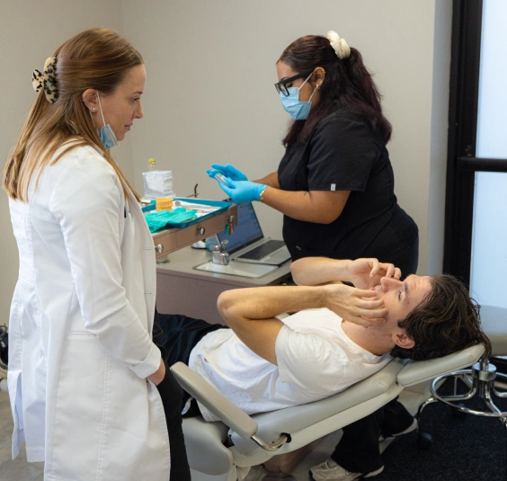 Two dental professionals examine a patient's teeth during an orthodontic consultation in a clinical setting.