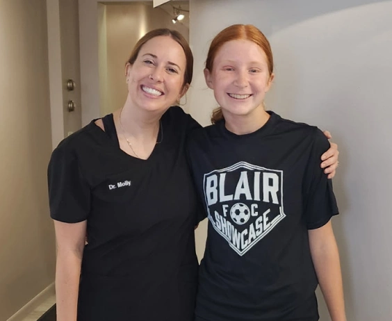 Two smiling women wearing black shirts pose together indoors at an orthodontics office.