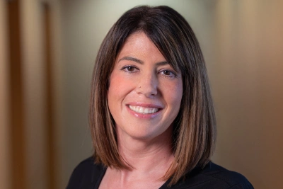 Professional woman smiling at camera in indoor office setting with neutral background.