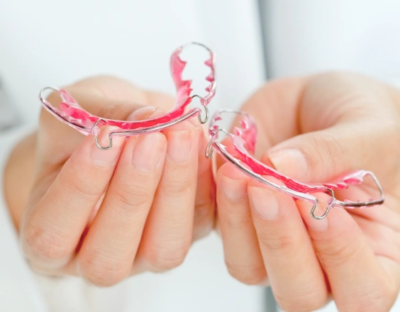 Person holding pink and clear orthodontic retainer against neutral background