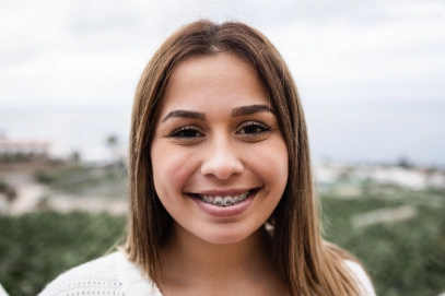 Smiling young woman with braces outdoors against a scenic landscape background.