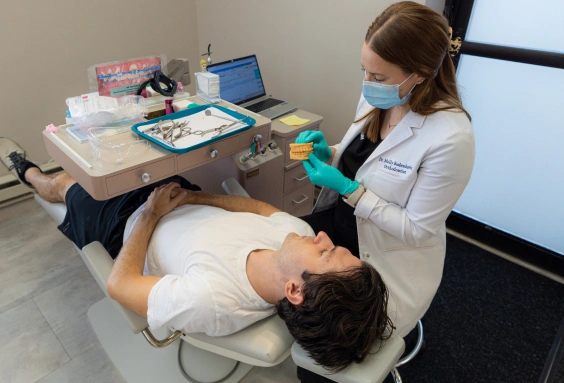 Orthodontist examining patient's teeth in clinical treatment room with dental equipment and tools.