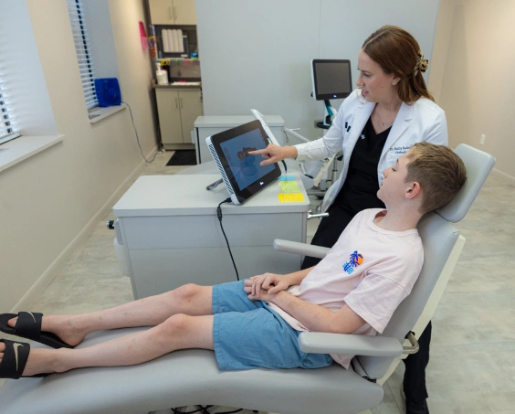 Orthodontist demonstrates digital scan technology to young patient in clinical treatment room.